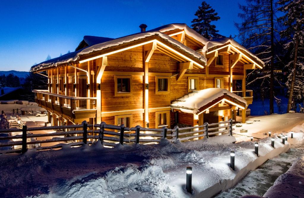 una cabaña de madera en la nieve por la noche en Chalet Migui Luxury Living & Spa *****, Crans Montana, en Crans-Montana