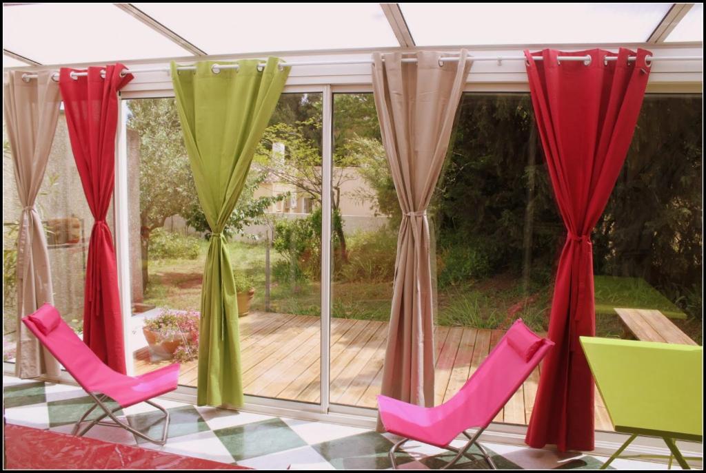 un porche cubierto con sillas y cortinas rojas y verdes en Gîte du Fenouil, en Lézignan-Corbières