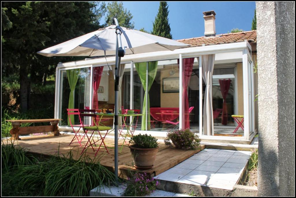 un salón acristalado con sombrilla en una terraza de madera en Gîte du Fenouil, en Lézignan-Corbières