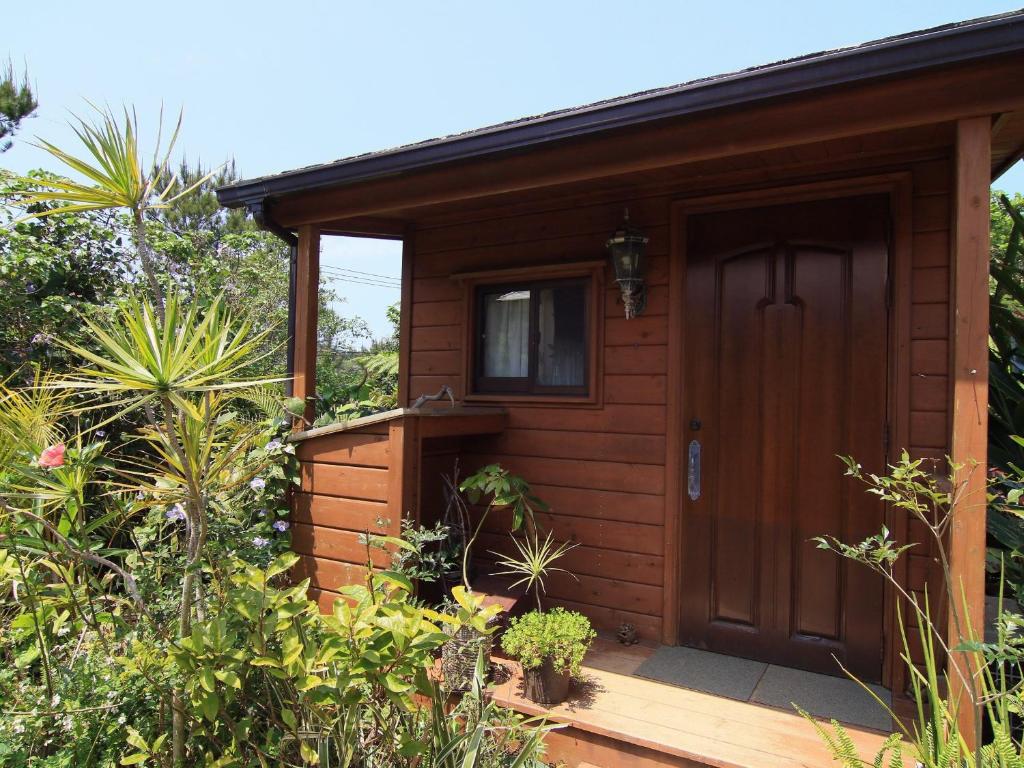 a small cabin with a wooden door in a garden at Yanbaru no mori -SEVEN Hotels and Resorts- in Ujimi