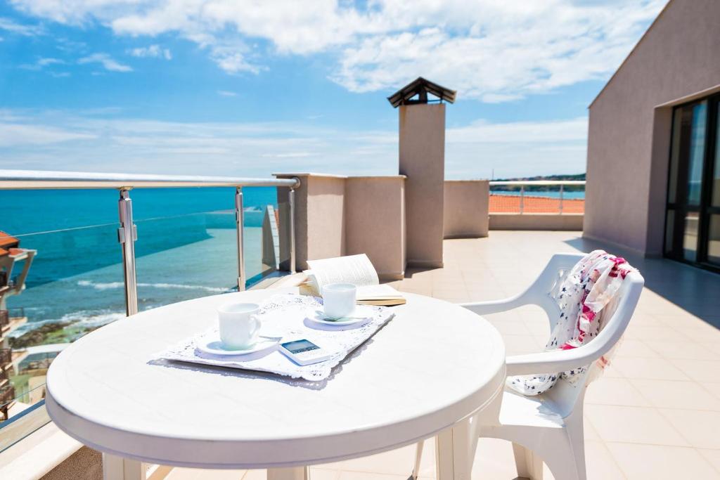 een witte tafel en stoelen op een balkon met uitzicht op de oceaan bij Amon Ra Hotel in Sozopol