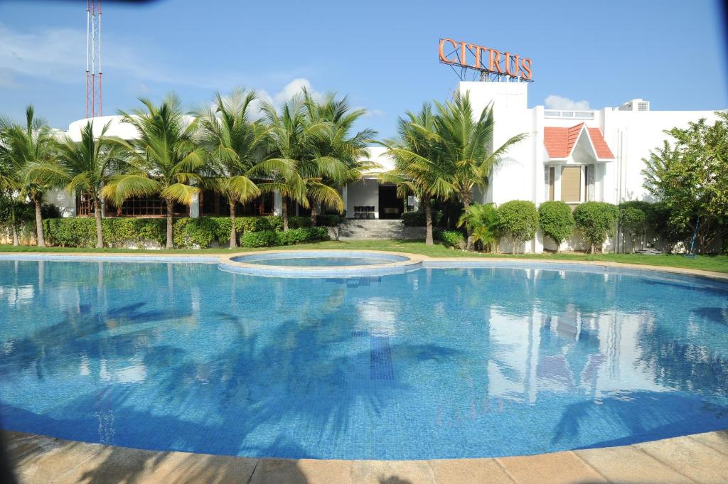 a large swimming pool with palm trees and a building at Vedic Village Sriperumbudur formerly known as Citrus Hotel in Sriperumbudur