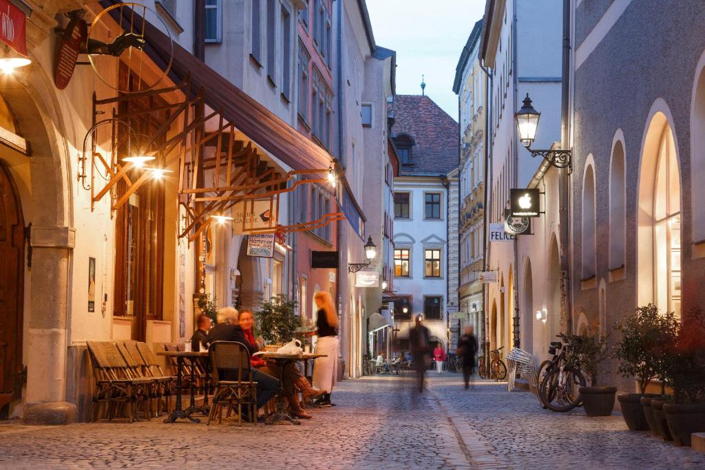 Un groupe de personnes assises à une table dans une rue la nuit dans l'établissement Hotel Orphée - Großes Haus, à Ratisbonne