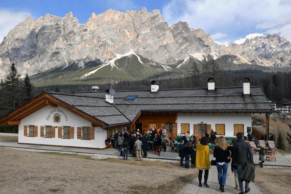 a group of people walking in front of a building with mountains at Jägerhaus Agriturismo in Cortina dʼAmpezzo