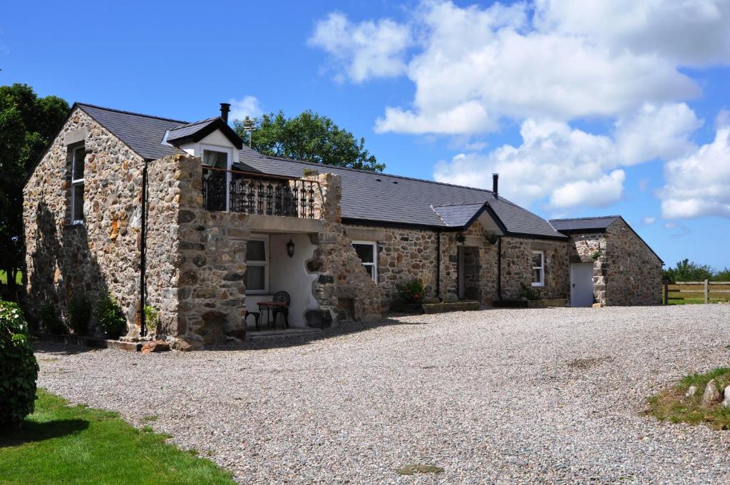 an old stone house with a gravel driveway at The Barn at Cae Bach in Gwalchmai