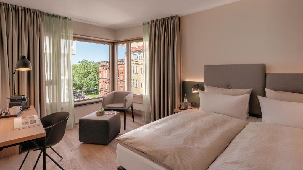 ベルリンにあるHotel the YARDのベッド、デスク、窓が備わるホテルルームです。
