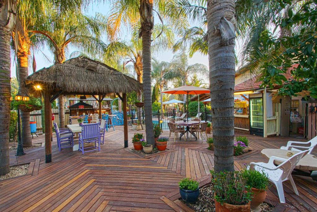 a wooden deck with chairs and tables and palm trees at Out of Africa Resort in Had Nes