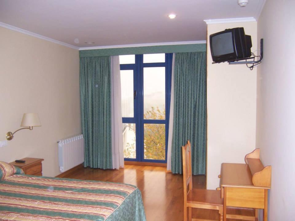 een slaapkamer met een bed, een tv en een raam bij Pensión Os Ancares in Becerreá