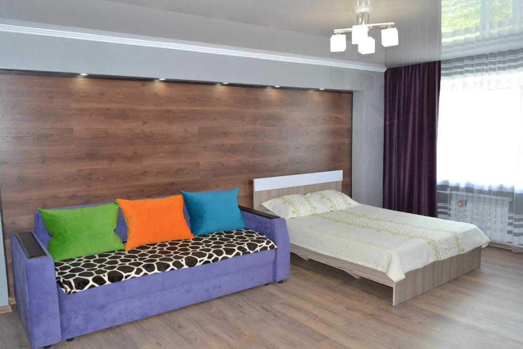 ein Schlafzimmer mit einem Bett und einer Bank mit bunten Kissen in der Unterkunft Хай-Тек апартаменты в центре по Гоголя51 in Qaraghandy