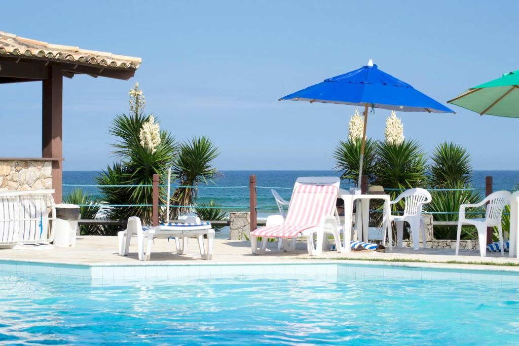 einen Pool mit Stühlen, Tischen und einem Sonnenschirm in der Unterkunft Pousada Oceano de Búzios in Búzios