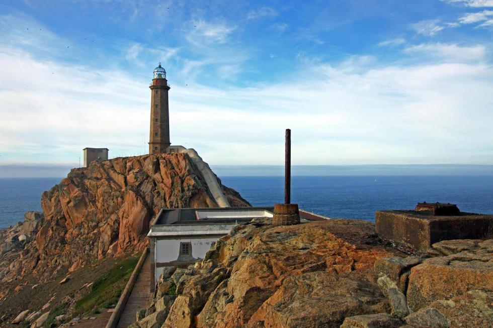 un phare au sommet d'une montagne avec l'océan dans l'établissement Pension Catro Ventos, à Camariñas