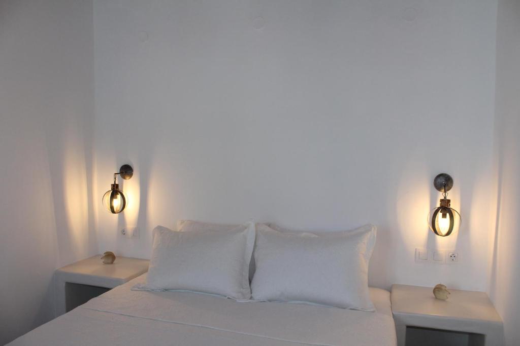 a white bed with white pillows and two lights at Studios Betty in Plaka Milou