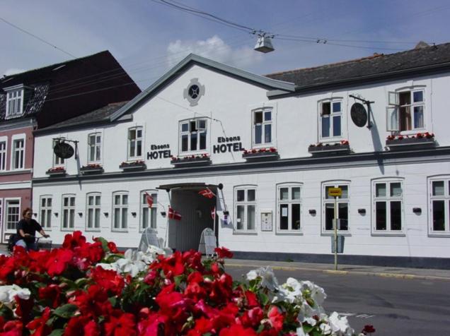 ein weißes Gebäude mit roten Blumen davor in der Unterkunft Ebsens Hotel in Maribo