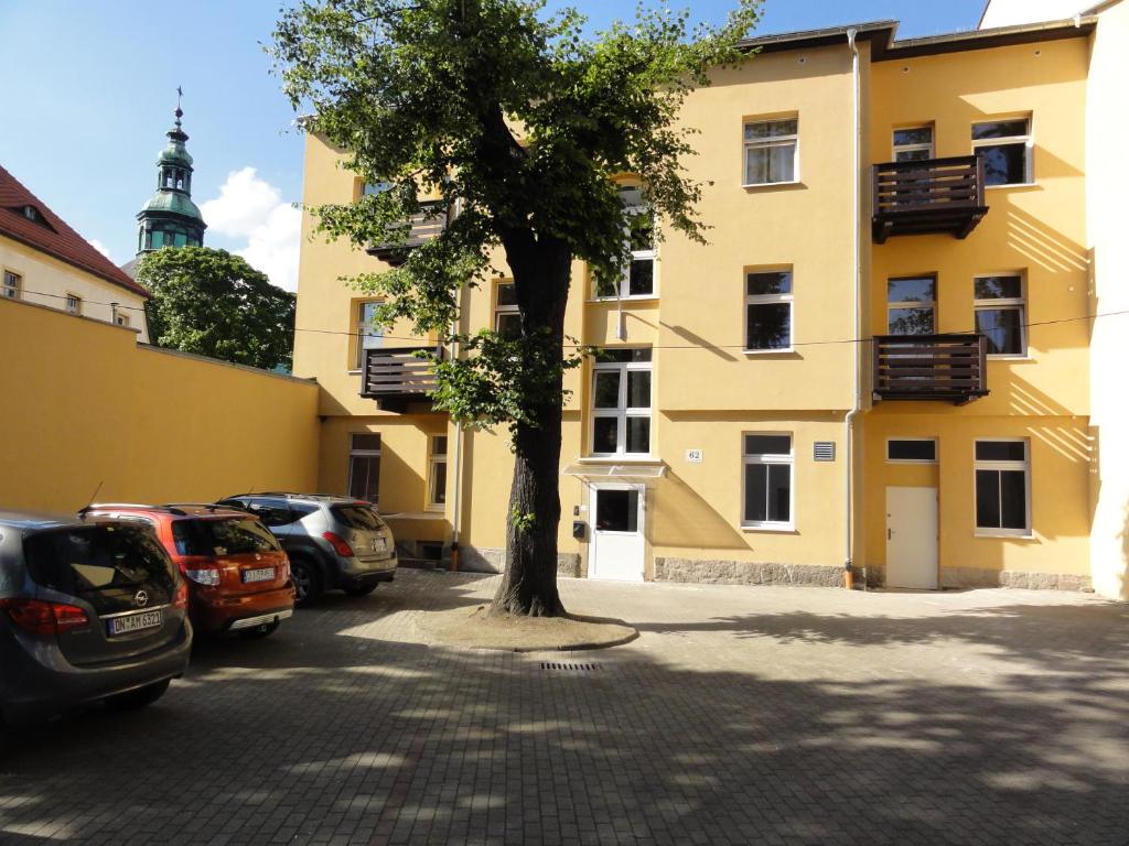 a tree in front of a yellow building with parked cars at Apartamenty EDK in Jelenia Góra