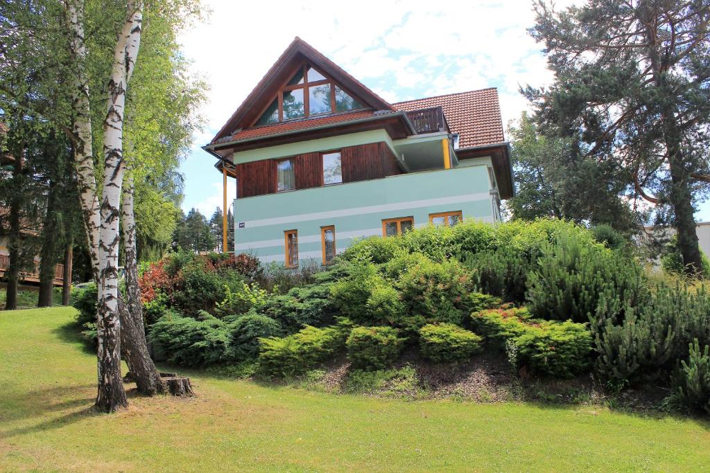 una casa blanca con techo marrón y algunos arbustos en Apartmany Riviera 505 en Lipno nad Vltavou