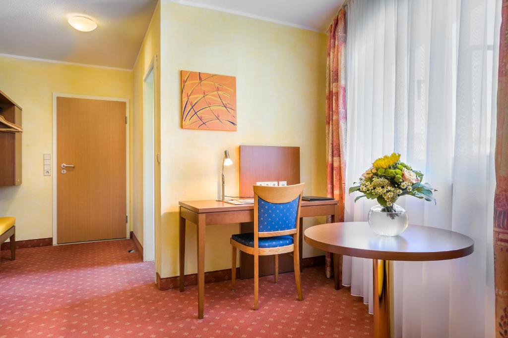 a room with a desk and a table with a vase of flowers at Hotel Rega Stuttgart in Stuttgart