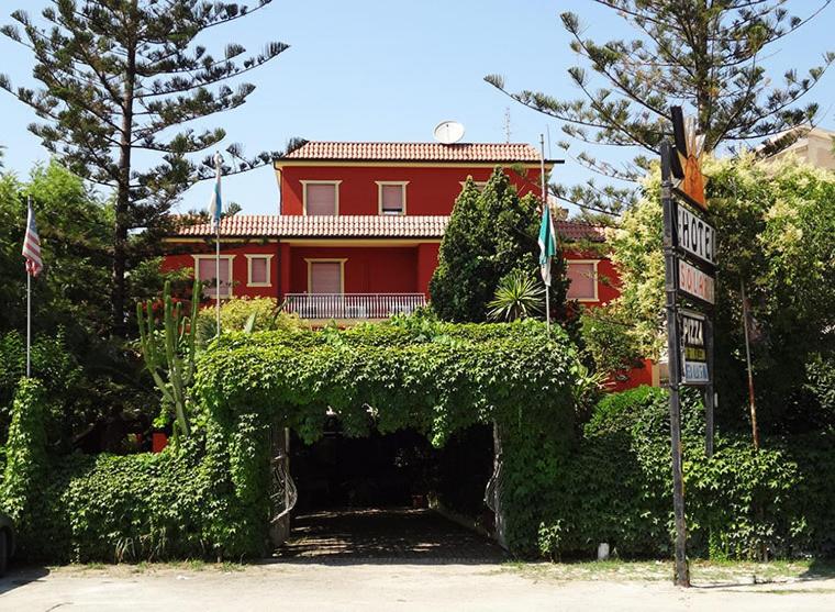 ein rotes Haus mit einer Hecke vor einem Gebäude in der Unterkunft Hotel Ristorante Solari in Briatico