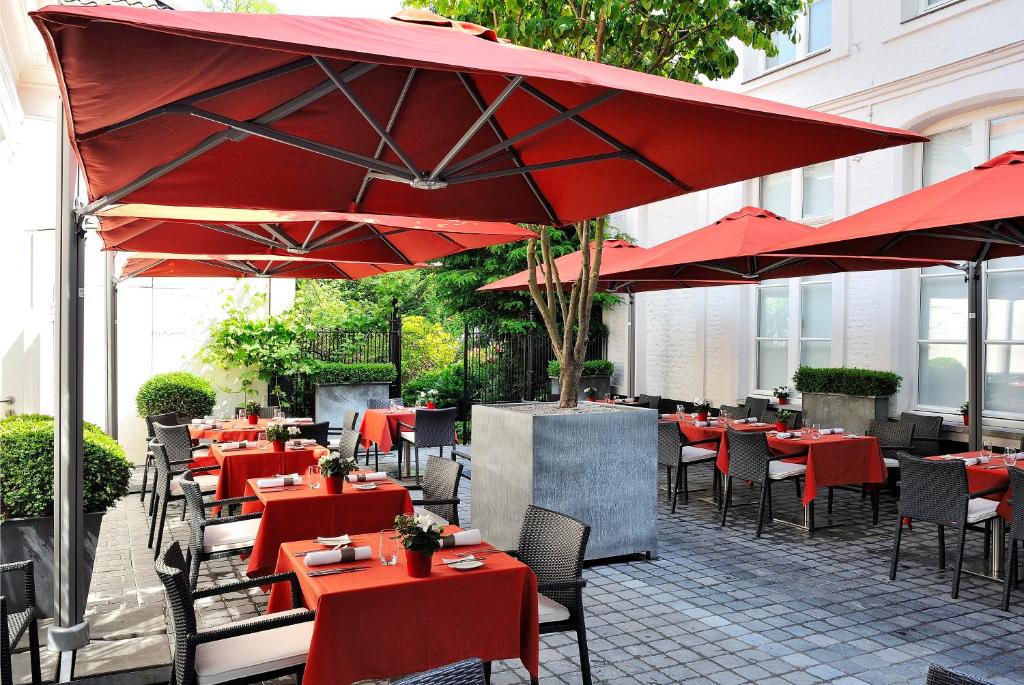 un restaurante con mesas rojas, sillas y sombrillas en Hotel Messeyne, en Cortrique