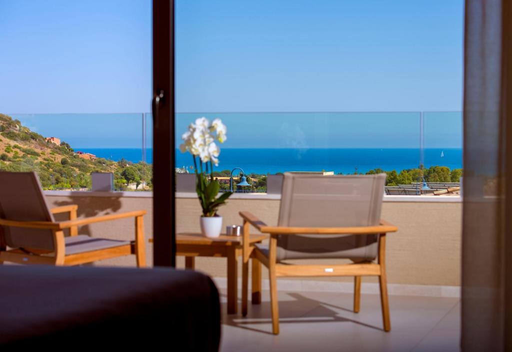 una camera con due sedie e un tavolo con vista sull'oceano di Domu Simius Hotel a Villasimius