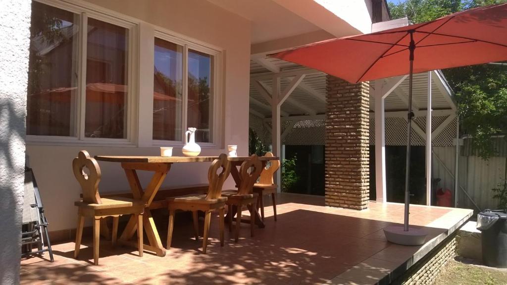 un patio con mesa, sillas y sombrilla roja en Eva vendégház, en Balatonlelle