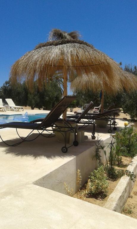 a straw umbrella and chairs and a pool at Menzel Churasco Djerba in Aghīr