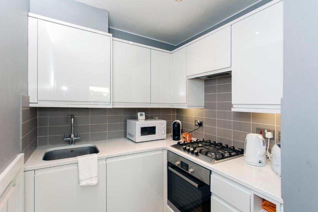 a kitchen with white cabinets and a sink and a microwave at ItalianFlat - Elsham in London