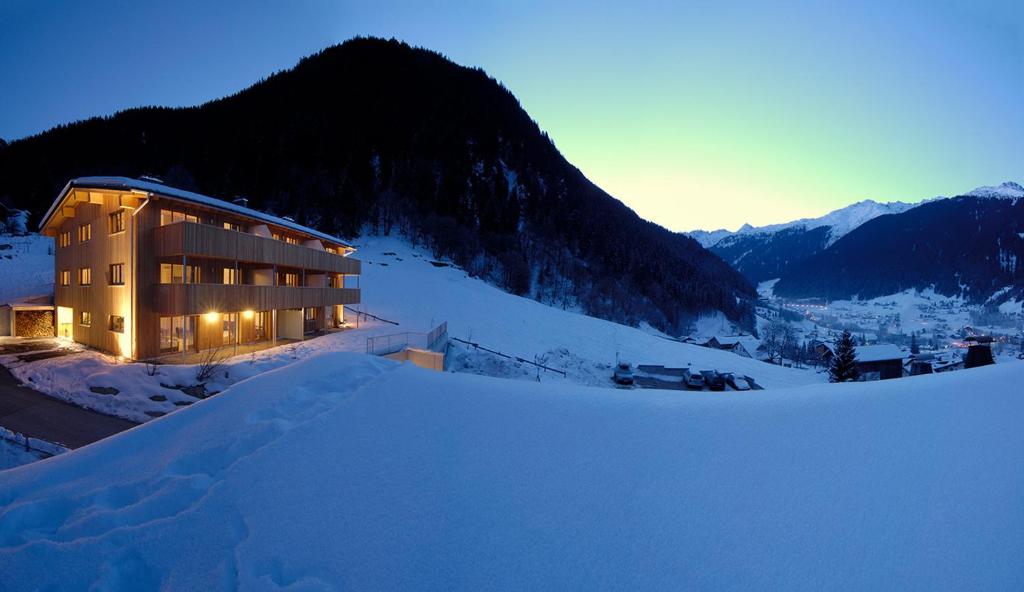 a building on a snow covered slope with a mountain at Montafon Chalets in Gaschurn