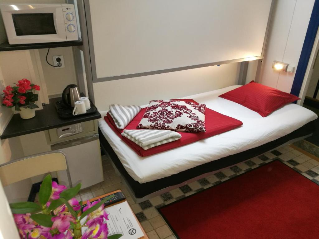 ein kleines Bett in einem kleinen Zimmer mit roten Kissen in der Unterkunft Stockholm Classic Budget Hotell in Stockholm