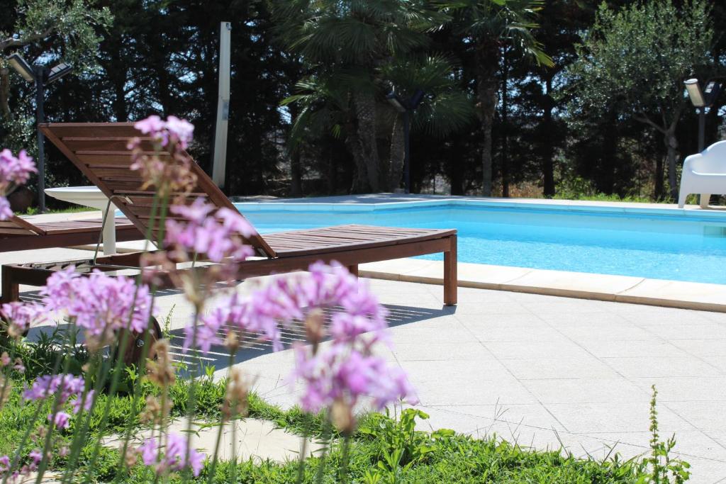 un banc à côté d'une piscine avec des fleurs violettes dans l'établissement Villa Orchidea Luxury B&B, à Ispica
