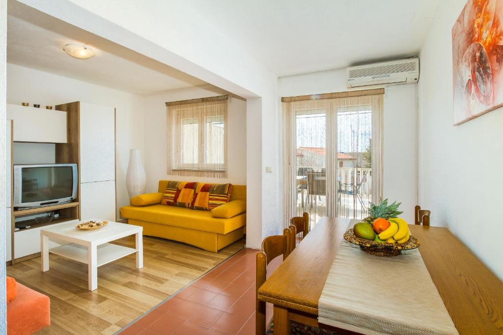 sala de estar con mesa y sofá amarillo en Apartmani Bregovec Maslenica, en Maslenica