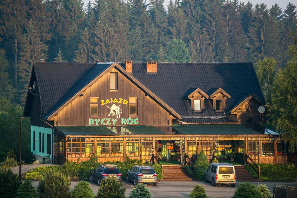 un gran edificio de madera con coches aparcados delante de él en Zajazd Byczy Róg, en Międzylesie