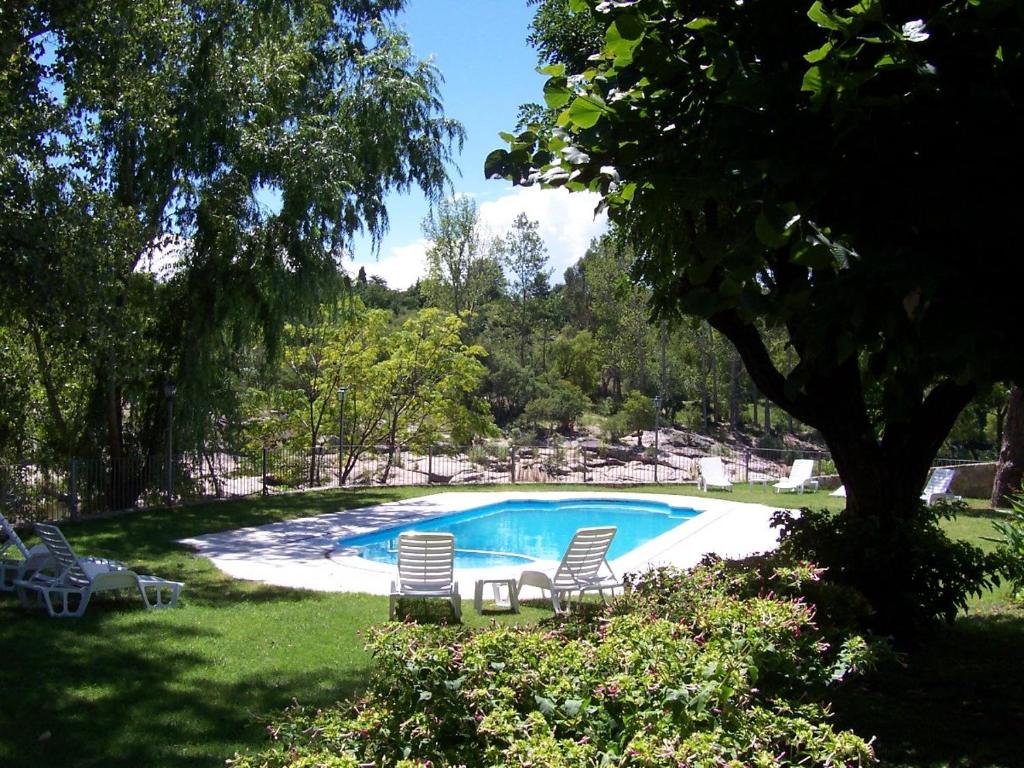 - une piscine avec deux chaises et un arbre dans l'établissement Costa Serrana Apart Hotel, à Mina Clavero