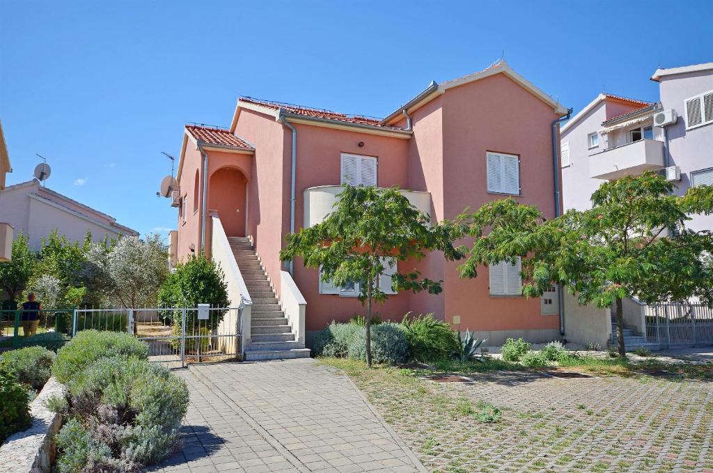 uma casa cor-de-rosa com escadas num quintal em Apartments Danica em Vodice