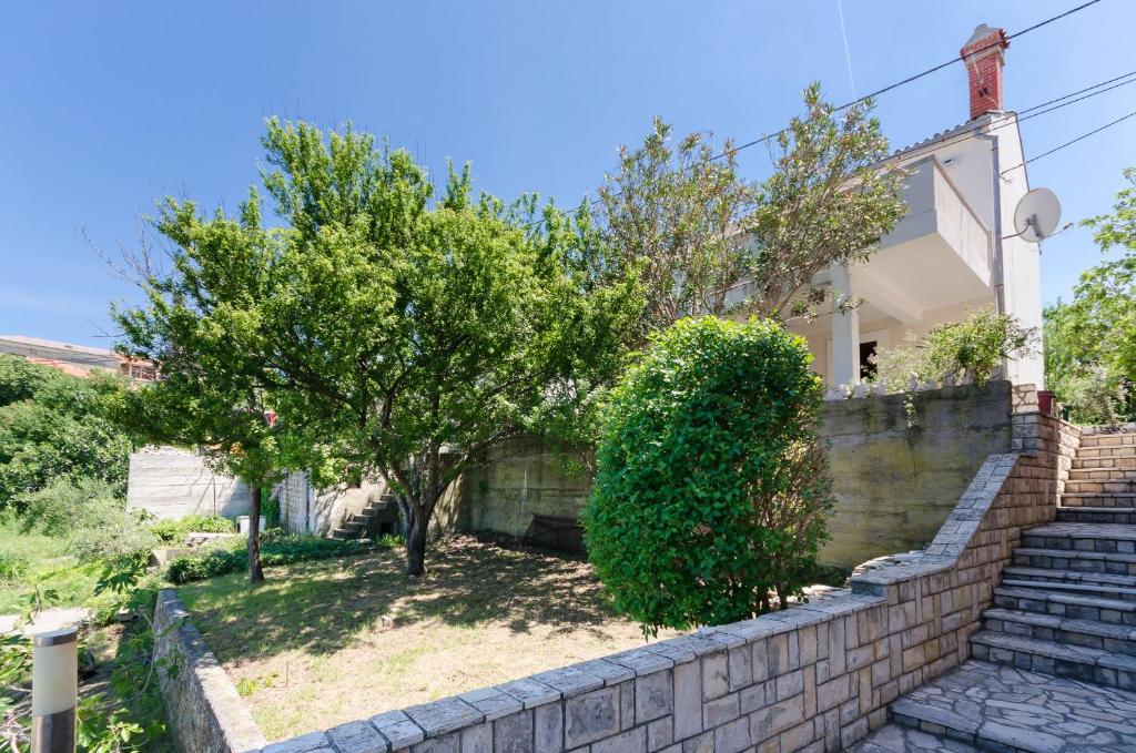 a house with a brick retaining wall and trees at Apartment RUZA in Lopar