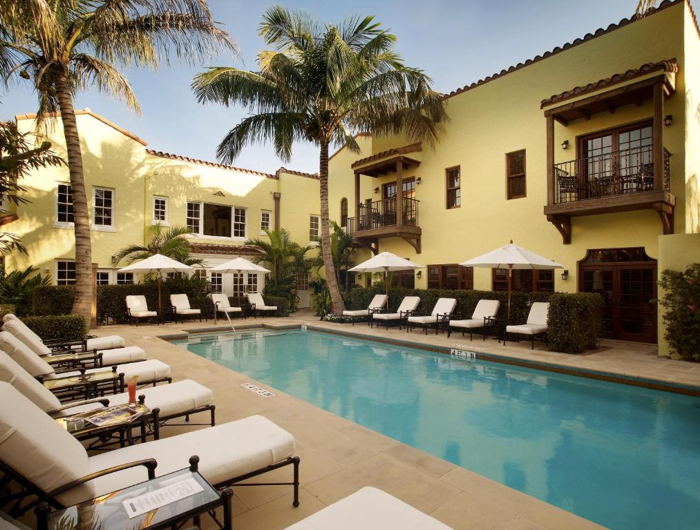 a resort pool with lounge chairs and palm trees at The Brazilian Court Hotel in Palm Beach