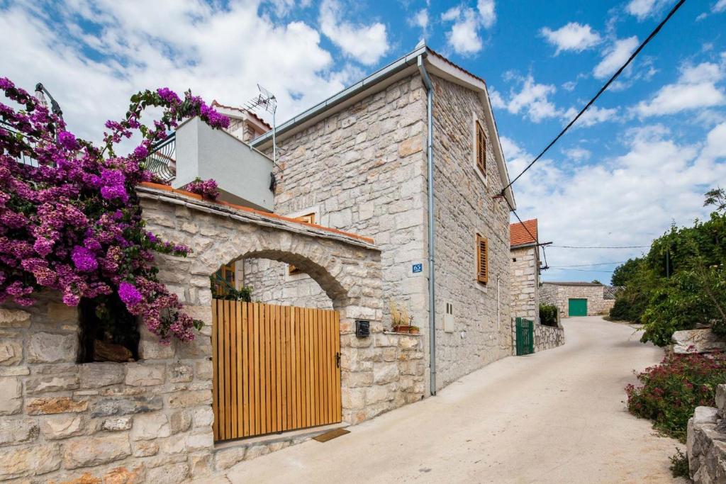 an old stone building with a gate and purple flowers at Apartment Zlendic in Gornje Selo