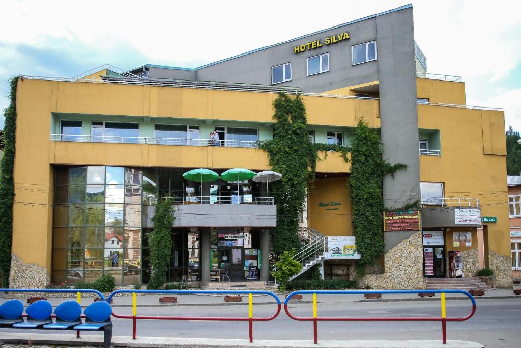 um edifício amarelo com mesas e guarda-chuvas à sua frente em Hotel Silva em Vatra Dornei