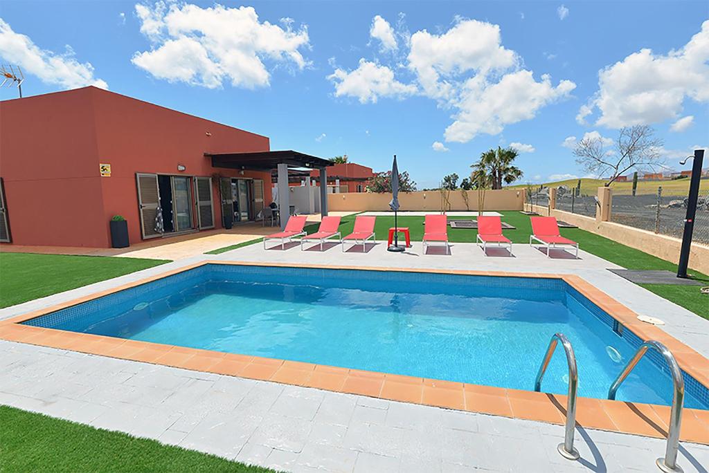 a swimming pool with chairs and a building at Villa Magna in Caleta De Fuste
