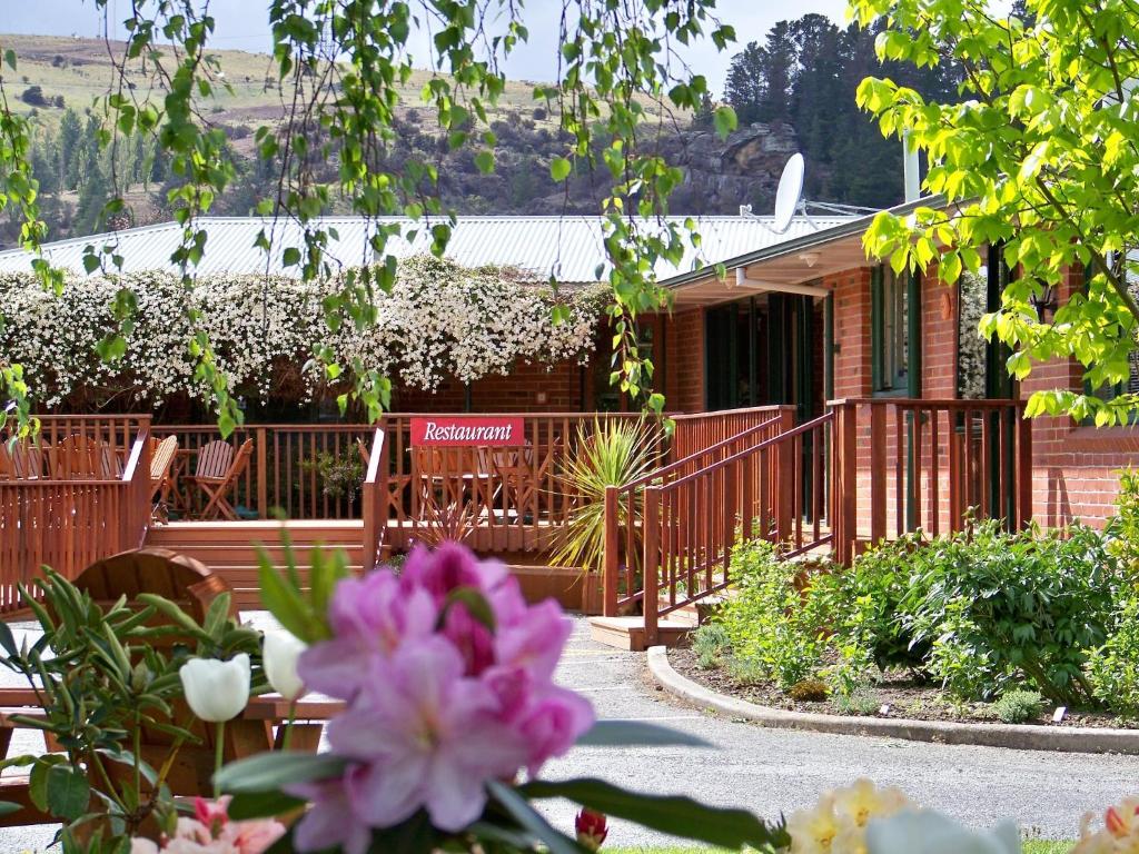 a house with a deck and flowers in front of it at Lake Roxburgh Lodge in Roxburgh