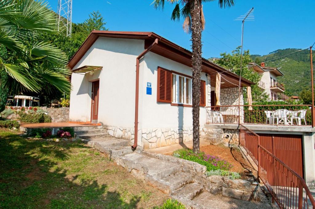 mały biały dom z czerwoną bramą i palmą w obiekcie House Mirella w mieście Mošćenička Draga