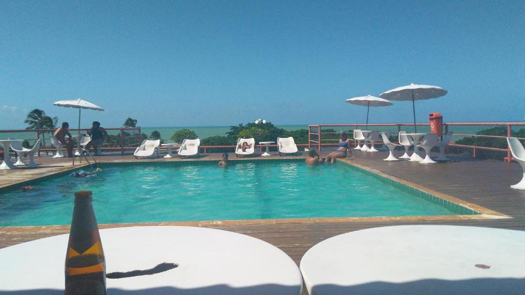 a swimming pool with chairs and umbrellas and the ocean at Victory Business Flat in João Pessoa