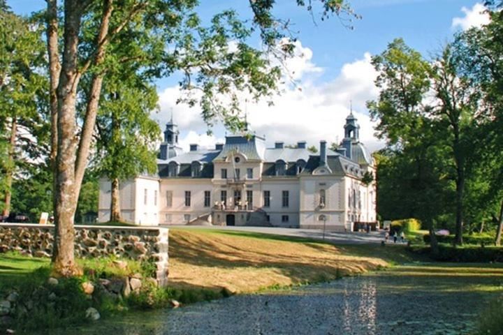 een groot wit huis met een vijver ervoor bij Kronovalls Vinslott in Skåne-Tranås