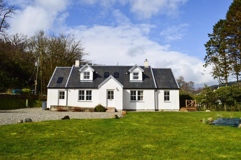 una casa bianca con un tetto nero su un cortile di Shelduck Cottage a Feorlean