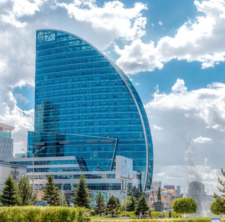 a tall glass building in front of a city at The Blue Sky Hotel and Tower in Ulaanbaatar