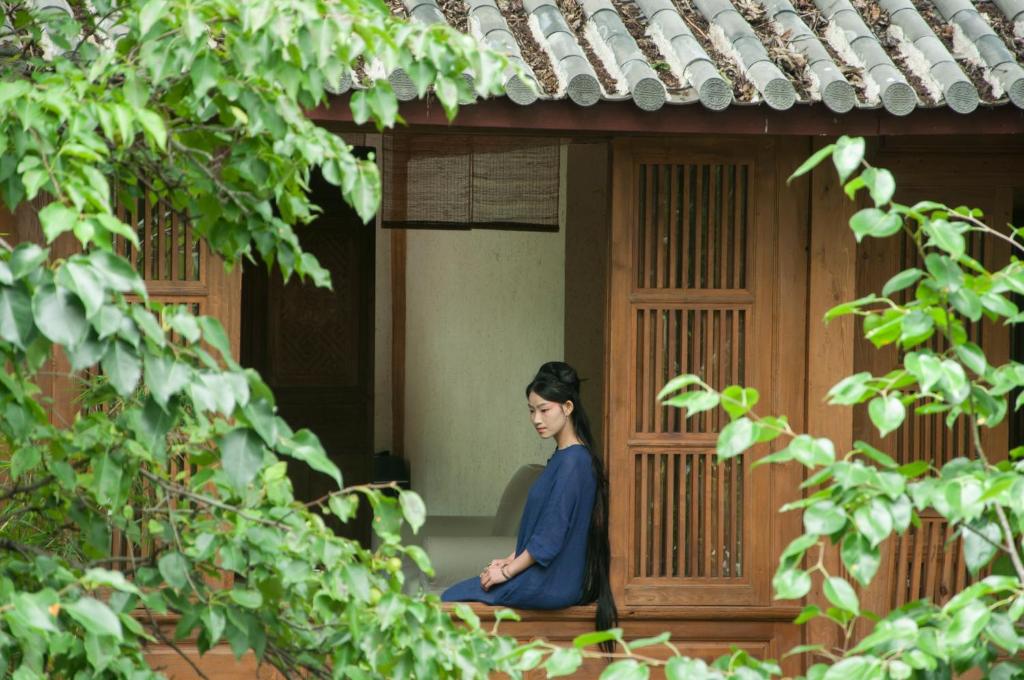 uma mulher sentada numa posição de meditação no alpendre de uma casa em 吾爱堂 em Lijiang