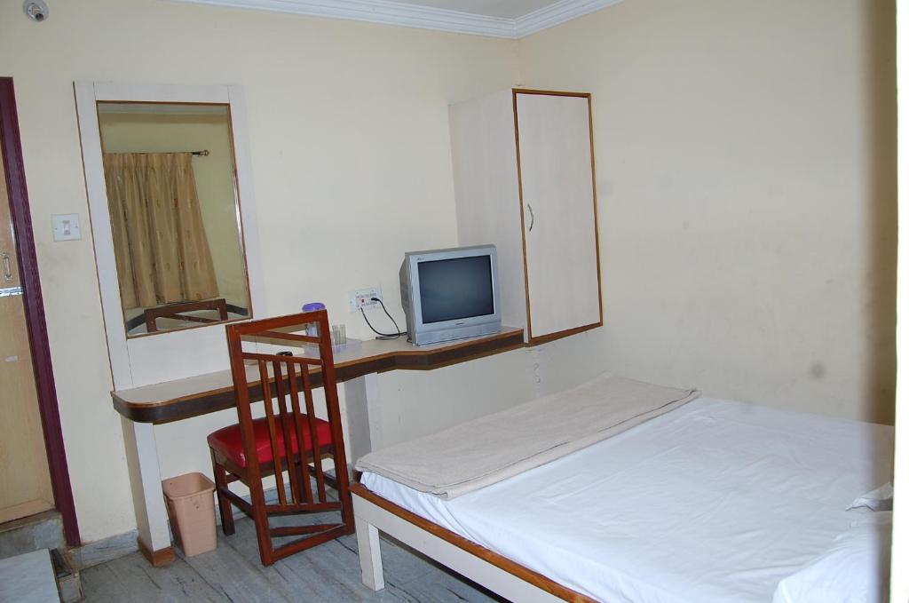 a bedroom with a bed and a desk with a television at Greens Residency in Bangalore