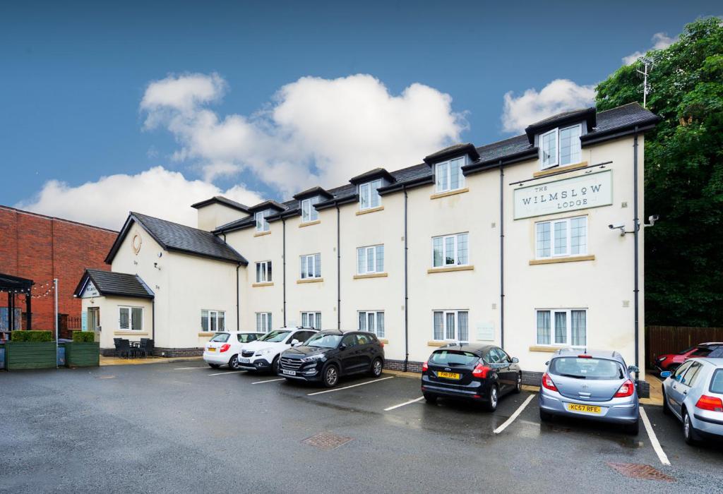 ein großes weißes Gebäude mit Autos auf einem Parkplatz in der Unterkunft Wilmslow Lodge in Wilmslow