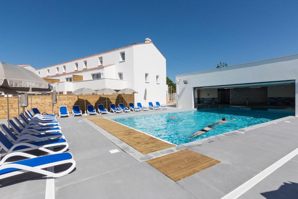 a swimming pool with lounge chairs and a building at Résidence Prestige Odalys Le Domaine des Pins in Noirmoutier-en-l'lle