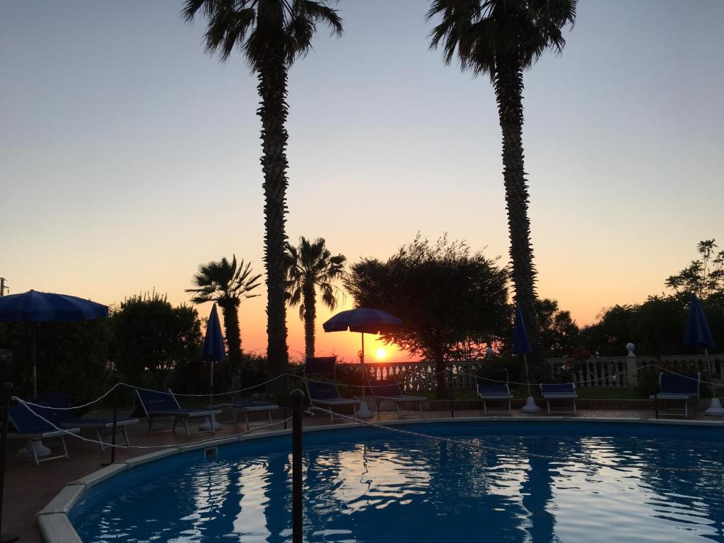 a pool with palm trees and a sunset in the background at My Villa Eden in Capo Vaticano