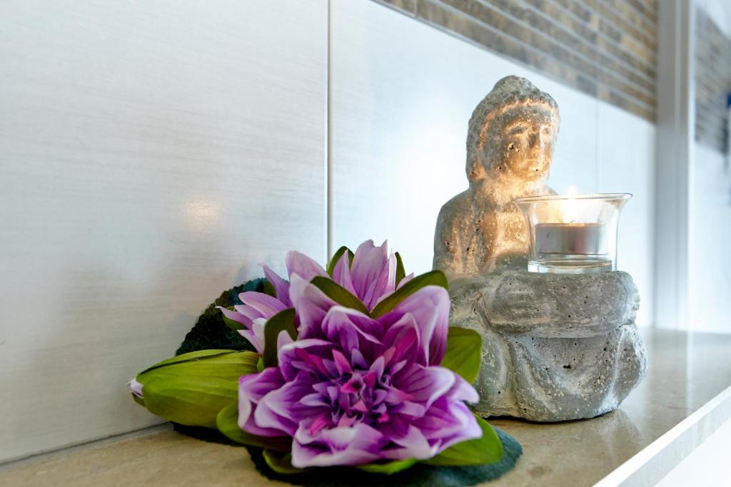 eine Statue und eine lila Blume auf einem Tisch mit einer Kerze in der Unterkunft Kühne's 4 Sterne Komfort-Apartments in Braunlage